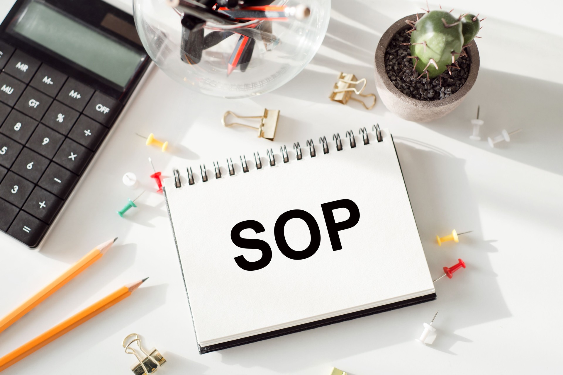 STANDARD OPERATION PROCEDURE SOP written in a white notepad near a calculator, pencils, glasses, a magnifying glass. Business concept